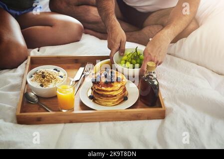 Das Frühstück im Bett ist immer eine gute Idee. Eine Aufnahme eines unverkennbaren Paares, das zu Hause im Bett zusammen frühstücken kann. Stockfoto