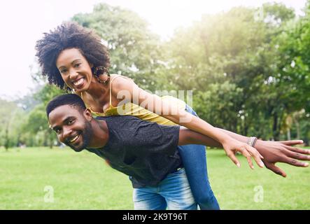 Er gibt mir das Gefühl, als könne ich fliegen. Beschnittenes Porträt eines hübschen jungen Mannes, der seine Freundin im Park huckert. Stockfoto