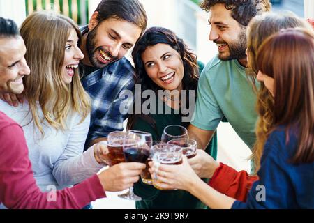 Freunde jubeln zusammen und toasten Bier und Wein stehen auf dem Balkon - - Freundschaftskonzept mit jungen Leuten, die Spaß haben, sich bei hom zu treffen Stockfoto