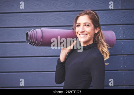 Im ab zum Workout. Verkürztes Porträt einer attraktiven jungen Sportlerin, die ihre Yogamatte trägt. Stockfoto