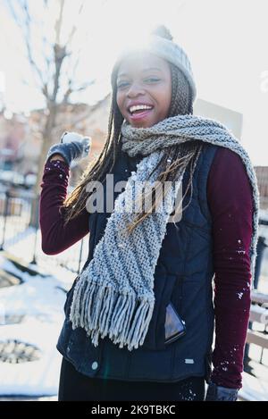 Du schaust dir den Schneeballkämpfer hier an. Eine schöne junge Frau wirft einen Schneeball an einem winterlichen Tag im Freien. Stockfoto