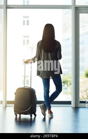 Endlich an meinem Ziel angekommen. Rückansicht einer nicht erkennbaren Frau, die aus dem Fenster auf einen Flughafen schaut. Stockfoto