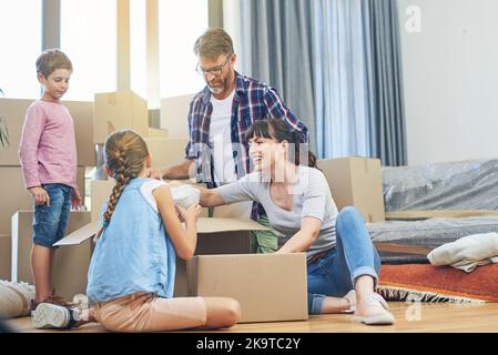 Wenn wir es zusammen tun, geht es schneller. Eine vierköpfige Familie hilft sich gegenseitig beim Packen von Boxen am Tag des Umzugsens. Stockfoto