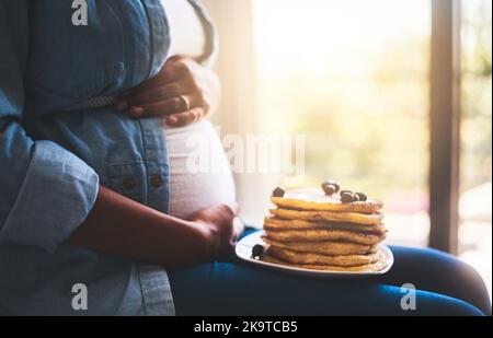 Beginnen Sie den Morgen mit etwas Süße. Eine Schwangerin, die zu Hause leckere Pfannkuchen isst. Stockfoto