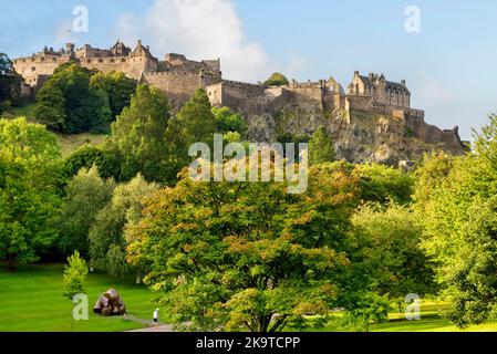 17. September 2022: Edinburgh, Schottland - das Edinburgh Castle, das auf seinem Felsen über den Bäumen der Princes Street Gardens thront. Jogger geht vorbei. Stockfoto