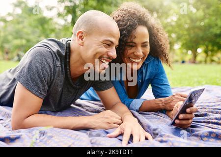 Technologie ist für jedermann, überall und jederzeit. Ein junges, schönes Paar, das den Tag in einem öffentlichen Park verbringt. Stockfoto