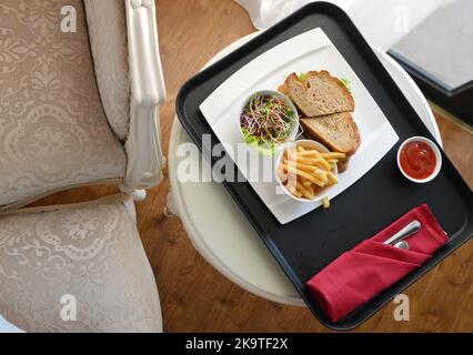 Gegrillte Rindersandwiches, serviert mit Beilagen von pommes Frites und Salat, auf einem Tablett mit Zimmerservice im Hotelzimmer Stockfoto