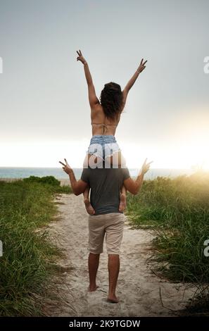 Liebe gibt dem Leben Sinn. Rückansicht eines glücklichen jungen Paares, das Spaß am Strand hatte. Stockfoto