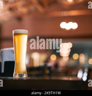 Bereit zum Erfrischen. Ein Glas Bier, das tagsüber an einem Tisch in einer Bierbrauerei steht. Stockfoto