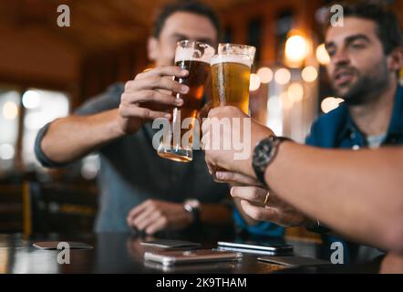 Heres zu einem erfolgreichen Unternehmen in der Zukunft. Drei fröhliche junge Männer, die feierlich mit Bier anstoßen, während sie an einem Tisch in einem Bier sitzen Stockfoto
