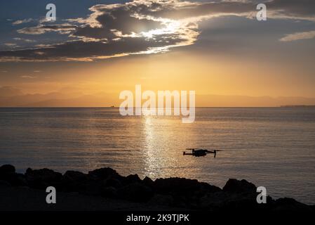 Silhouette Der Drohne, Die Über Den Pier Fliegt. Sonnenaufgang Von Der Insel Korfu Mit Blick Auf Die Berge Der Balkanhalbinsel Griechenlands, Moraitika, Korfu, Griechenland Stockfoto