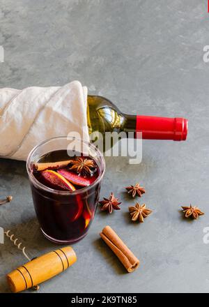 Glühweingetränk, Rotwein-Flasche und verschiedene Gewürze auf grauem Beton-Hintergrund. Perfektes Wintergetränk für kalte Tage. Draufsicht Stockfoto