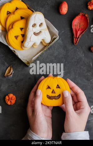 Weibliche Hände halten Kürbis unheimlich Gesicht Cookie auf dunklem Hintergrund mit halloween-Symbol Sand Dekoration. Happy Halloween Konzept. Stockfoto