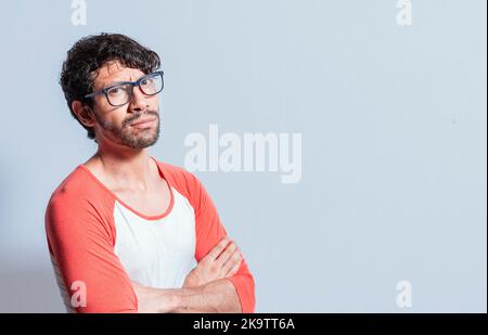 Junger latein in einer Brille mit gekreuzten Armen, der im Profil auf die Kamera blickt. Nicaraguanischer Mann mit gekreuzten Armen, der isoliert auf die Kamera schaute Stockfoto