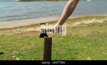 Mann mit tätowierten Armen, die Holz mit einer kleinen Axt hacken. Stockfoto