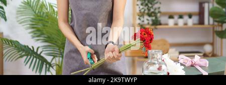 Floristen-Konzept, weibliche Floristen schneiden Stiele von roten Gerbera mit Schere für die Herstellung Blumenstrauß. Stockfoto