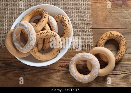 Blick aus der Höhe auf verschiedene hausgemachte Bagels in einer weißen Schüssel auf dem Tisch Stockfoto