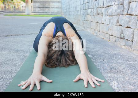 Junge hispanische Frau macht Yoga auf der grünen offenen Matte im Freien. Konzept für Fitness o Yoga. Speicherplatz kopieren. Stockfoto