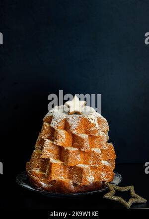 Italienische Weihnachtskuchen Pandoro verziert mit süßen Stern auf dem schwarzen Hintergrund. Wunderschönes Weihnachtsessen-Konzept. Speicherplatz kopieren. Stockfoto