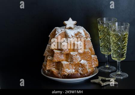 Nahaufnahme von Pandoro, italienischer Weihnachtskuchen mit weihnachtsdekoration und Champagner auf schwarzem Hintergrund. Wunderschönes Weihnachtsessen-Konzept. Stockfoto