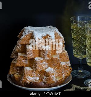 Nahaufnahme von Pandoro, italienischer Weihnachtskuchen mit weihnachtsdekoration und Champagner auf schwarzem Hintergrund. Wunderschönes Weihnachtsessen-Konzept. Stockfoto