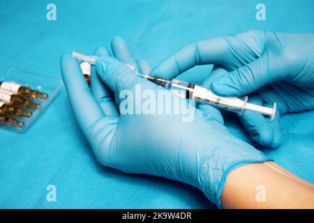 Hände einer Krankenschwester in Handschuhen halten eine Spritze Stockfoto
