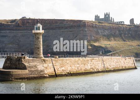 WHITBY, Großbritannien - 21. September 2022. Whitby Hafenmauer mit Leuchtturm. Whitby Abbey Ruinen im Hintergrund. Stockfoto