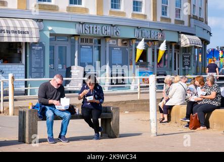 WHITBY, Großbritannien - 21. September 2022. Menschen, die auf einer Bank vor einem Fish and Chip Shop in Whitby Harbour, North Yorkshire, Fisch und Chips essen Stockfoto