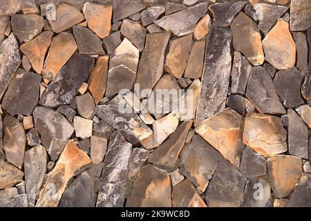 Ein grauer gelber Steinwall aus Steinplatten und Sandsteinplatten Hintergrund, holprige Steinwand Textur, Rocky Struktur Hintergrund Stockfoto