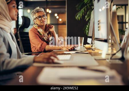 Geschäftsleute, die ein Gespräch führen, während sie an ihrem Schreibtisch in einem Büro arbeiten. Zwei verschiedene Geschäftsfrauen arbeiten als Team in einem kreativen Team Stockfoto