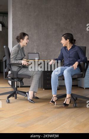 Zwei lachende Frauen saßen am Arbeitsplatz auf Stühlen Stockfoto