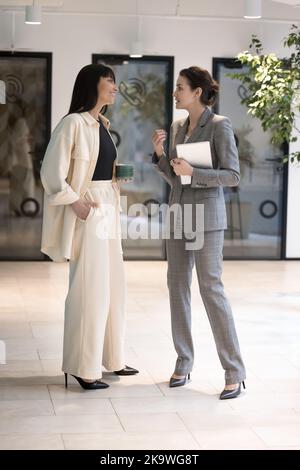 Zwei Geschäftsfrauen, die im modernen Büro stehen und sprechen Stockfoto