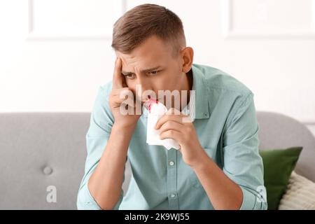 Junger Mann mit Nasenbluten und Gewebe zu Hause Stockfoto