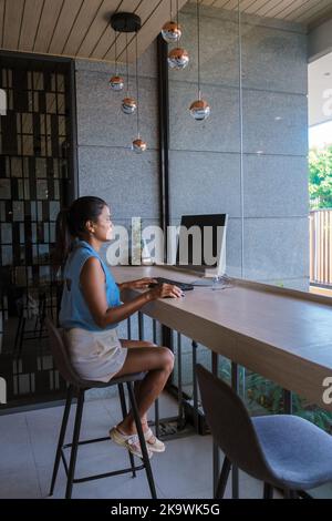 Thailändisch-asiatische Frauen, die an einem Computertisch in einer Hotellobby arbeiten. Stockfoto