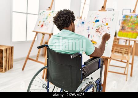 Junger afroamerikanischer behinderter Künstlermann, der im Kunststudio auf dem Rollstuhl sitzt und zeichnet. Stockfoto