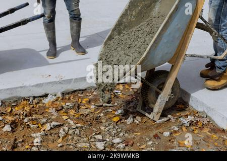 Bauarbeiter gießt Zement von Schubkarre auf, um einen neuen Bürgersteig an der Seite des Hauses zu schaffen Stockfoto