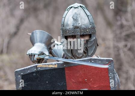 Edler Krieger. Porträt eines medeival Krieger oder Ritter in Rüstung und Helm mit Schild und Schwert posiert isoliert über dunklen Hintergrund. Stockfoto