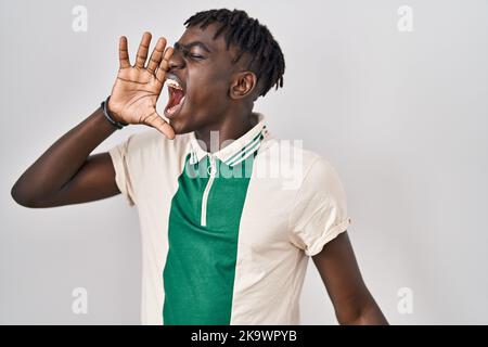 Afrikanischer Mann mit Dreadlocks, der über einem isolierten Hintergrund steht und laut auf der Seite mit der Hand auf dem Mund schreit. Kommunikationskonzept. Stockfoto