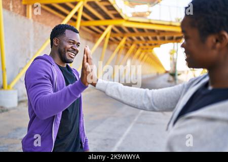 Mann und Frau, die auf der Straße hochgezogene Hände tragen, tragen Sportswear High Five Stockfoto