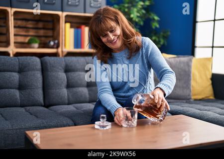 Frau mittleren Alters gießt Lakritze auf Glas sitzen auf dem Sofa zu Hause Stockfoto