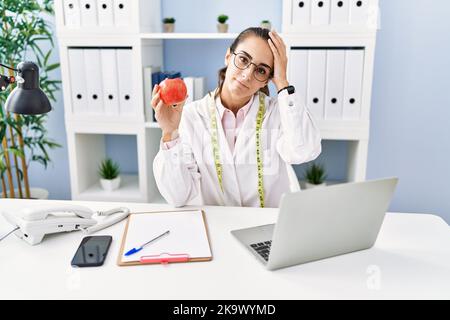 Junge hispanische Frau, die in der Ernährungsklinik arbeitet, gestresst und frustriert mit Hand auf Kopf, überrascht und wütend ins Gesicht Stockfoto