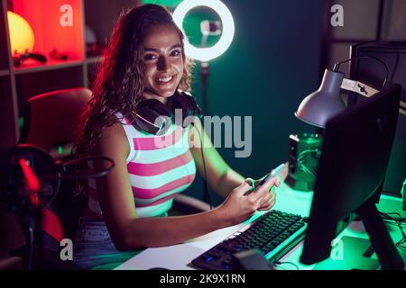 Junge schöne hispanische Frau streamer mit Computer und Smartphone im Spielzimmer Stockfoto