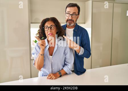 Das Paar mittleren Alters, das zusammen steht und besorgt und nervös mit dem Zeigefinger zur Seite zeigt, besorgt und überrascht den Ausdruck Stockfoto