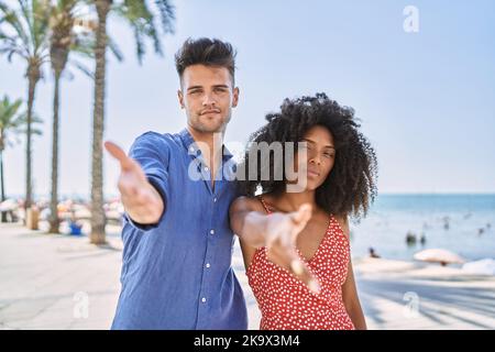 Junge interrassische Paar im Freien an einem sonnigen Tag lächelnd freundlich bietet Handschlag als Begrüßung und einladend. Erfolgreiches Geschäft. Stockfoto
