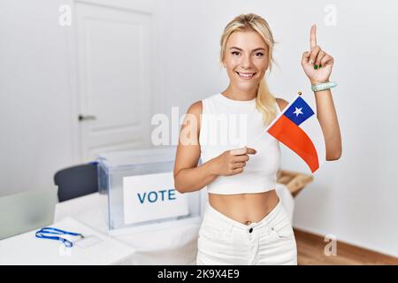 Die junge kaukasische Frau bei den politischen Wahlkampfwahlen hält die chilenische Flagge mit einem Lächeln und einer Idee oder Frage, die mit dem Finger mit einem glücklichen Gesicht zeigt, Nummer eins Stockfoto