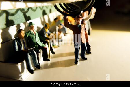 Miniaturspielzeug von Personen, die von der Arbeit an einem öffentlichen Verkehrskonzept mit abendlicher gelblicher Seitenbeleuchtung reisen - Reisen Sie mit dem Zug oder Bus. Stockfoto