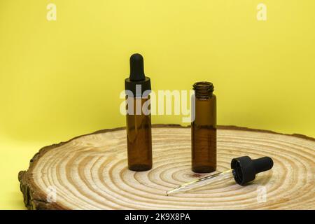 Modell aus braunen Glasfläschchen mit Tropferdeckel auf Holzbrett und gelbem Hintergrund. Zwei leere Glasflaschen und Pipette. Konzept von Körper und Gesicht c Stockfoto