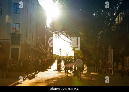 Hintergrundbeleuchtetes Szenenbild einer Kopfsteinpflasterstraße, die zum Rhein Rhiver in der historischen Düsseldorfer Altstadt führt. Am späten Nachmittag Herbstsonne. Stockfoto