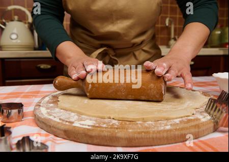 Cropped view die Hände der Hausfrau Rollen den Teig aus, verwenden ein Nudelholz und kochen Lebkuchen in der Küche Stockfoto