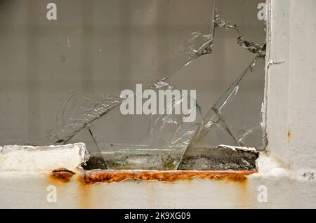 Schäden in der Ecke eines Fensters mit Rost am Rahmen und Rissen im Glas Stockfoto
